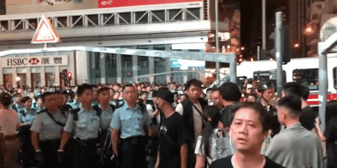 Police officers violently pull off civilians’ face-masks, threatening to beat them up.